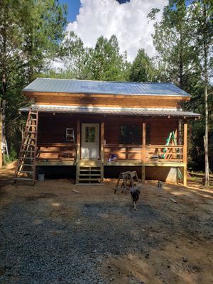 Cabin under construction with metal roof and wooden deck.