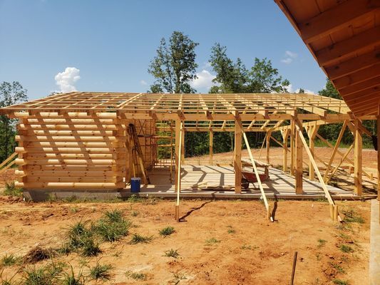 Log cabin and wooden structure under construction with blue sky background.