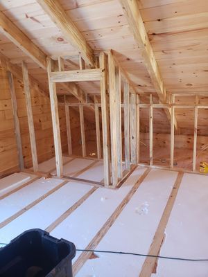 Interior framing of a room with exposed wooden studs, rafters, and insulated floor.