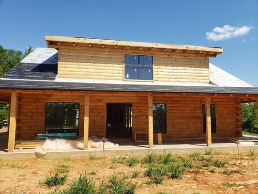 Two-story log cabin under construction with a porch and windows.