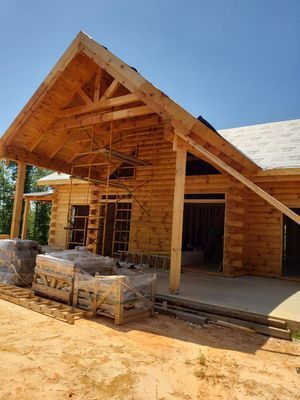Log cabin under construction with a wooden roof, scaffolding, and materials.