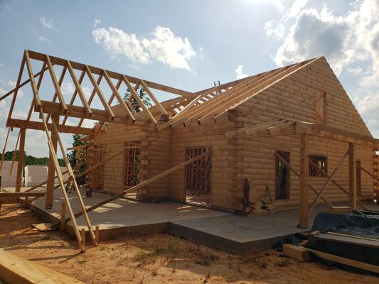 Log cabin under construction with exposed wooden beams, blue sky background.