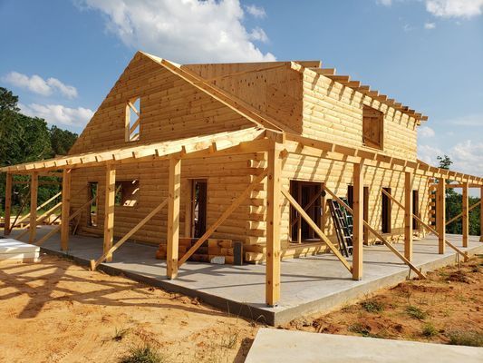 Wooden house under construction with porch on a concrete slab, set against a blue sky.
