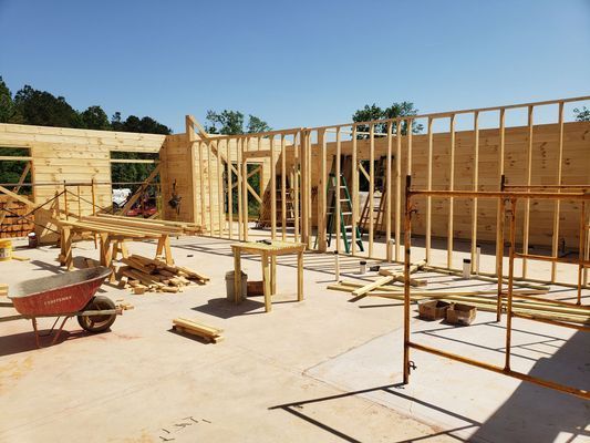 Construction site: wooden frame walls partially built on a concrete foundation, lumber scattered about.