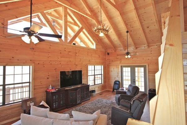Interior of a log cabin living room with wooden walls, a high ceiling, and a television.