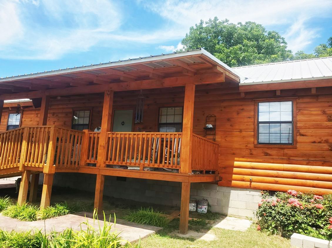 Log cabin with wooden porch and railing, metal roof, on a sunny day.