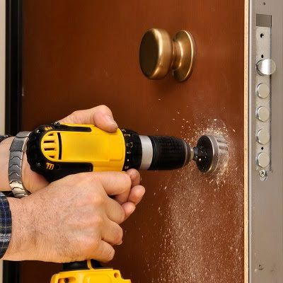 A man is using a drill to fix a door lock.