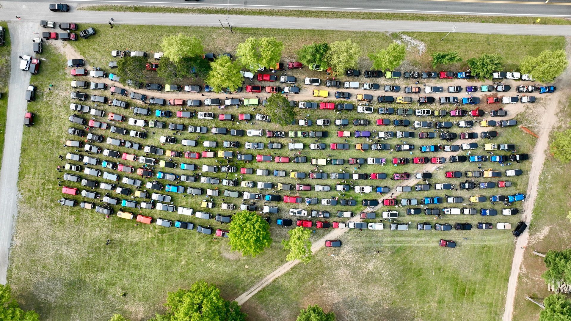 Aerial view of many cars parked on grass in rows.