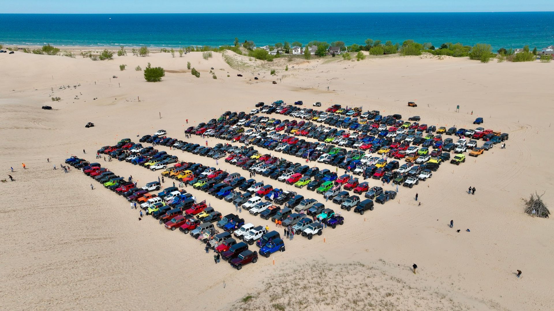 Cars parked on a sandy beach. Many vehicles in rows with ocean in the background.