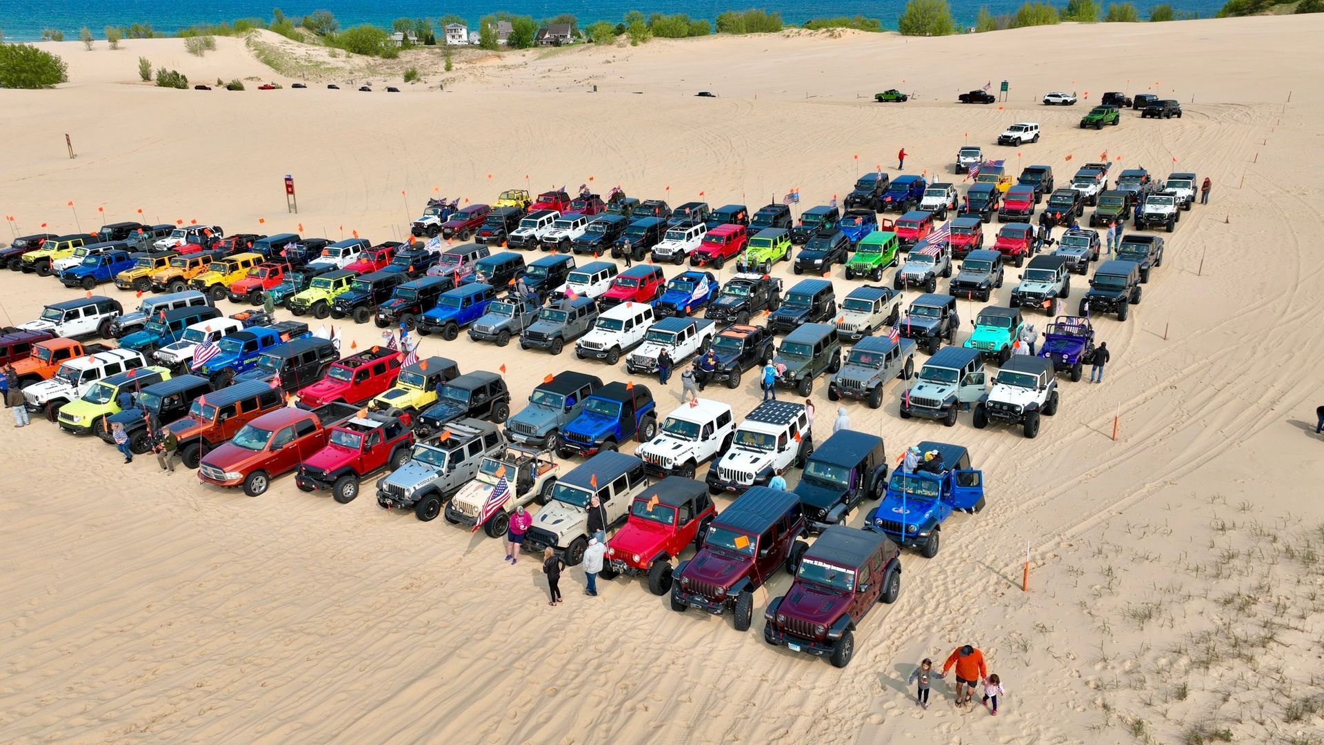 A large group of Jeeps parked on a sandy beach. Many colors, formation appears to be a heart shape.