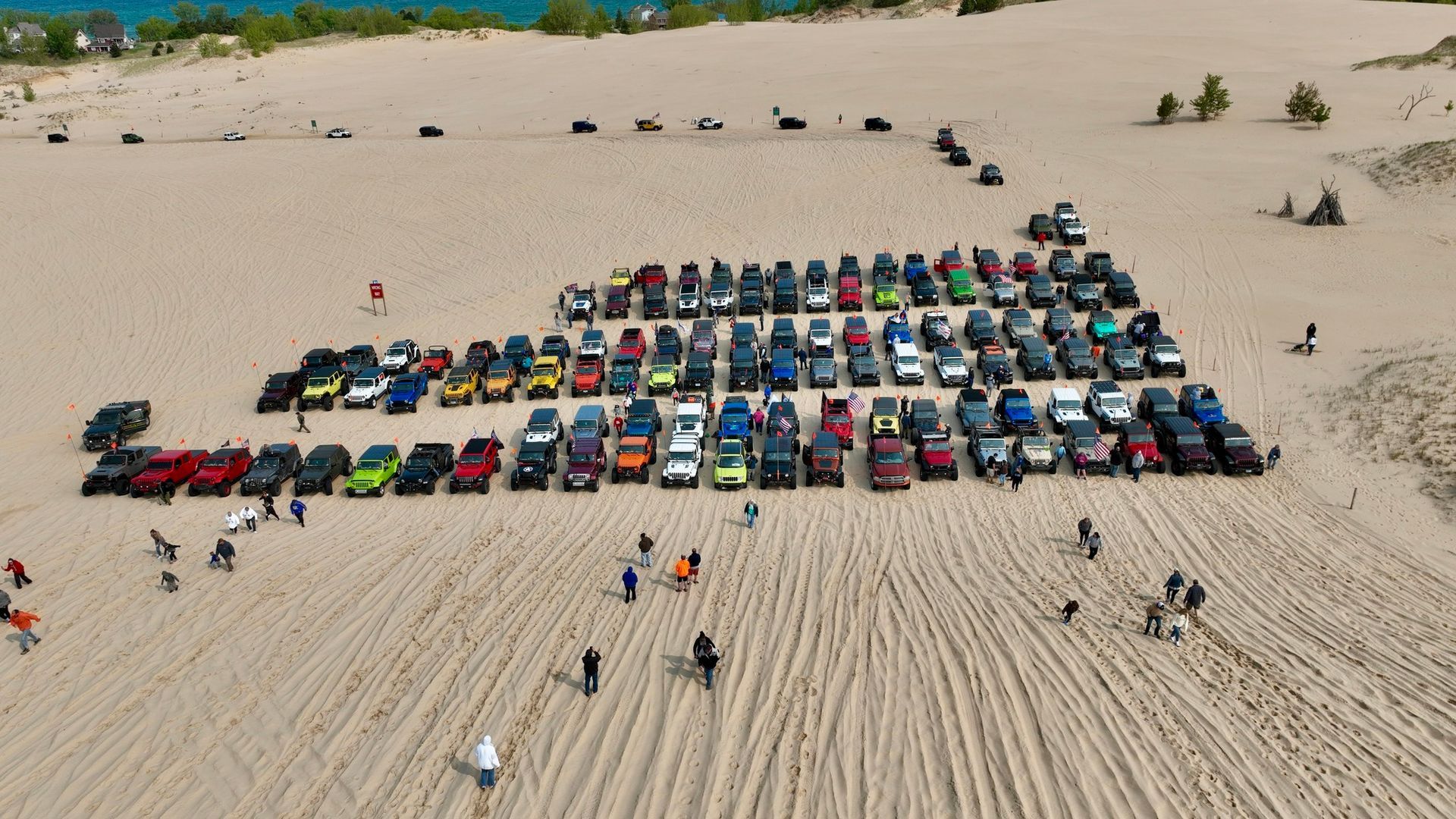 Group of Jeeps parked on a sandy dune; people standing nearby.