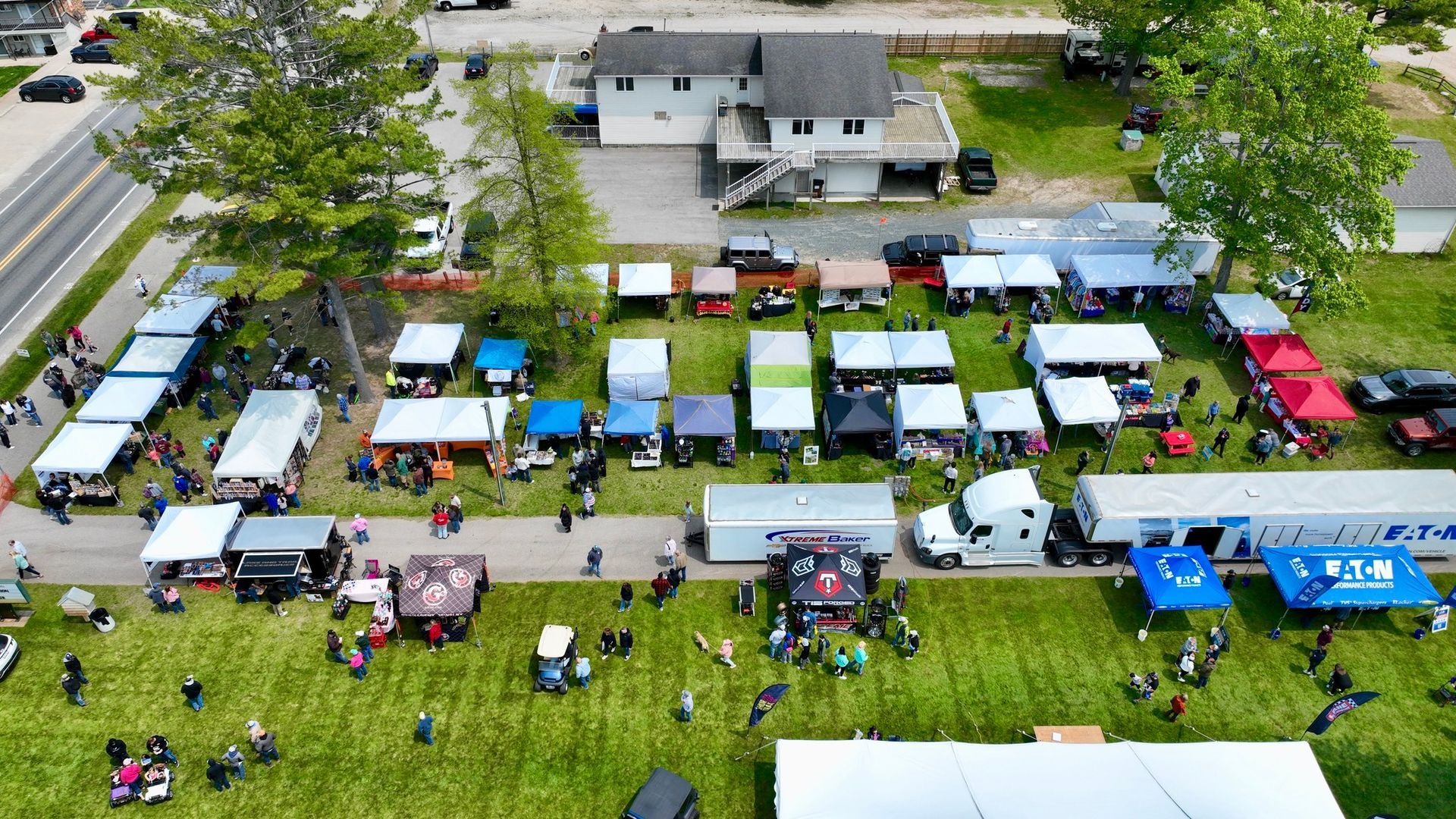 Aerial view of an outdoor market with vendor tents, customers, and a few buildings.