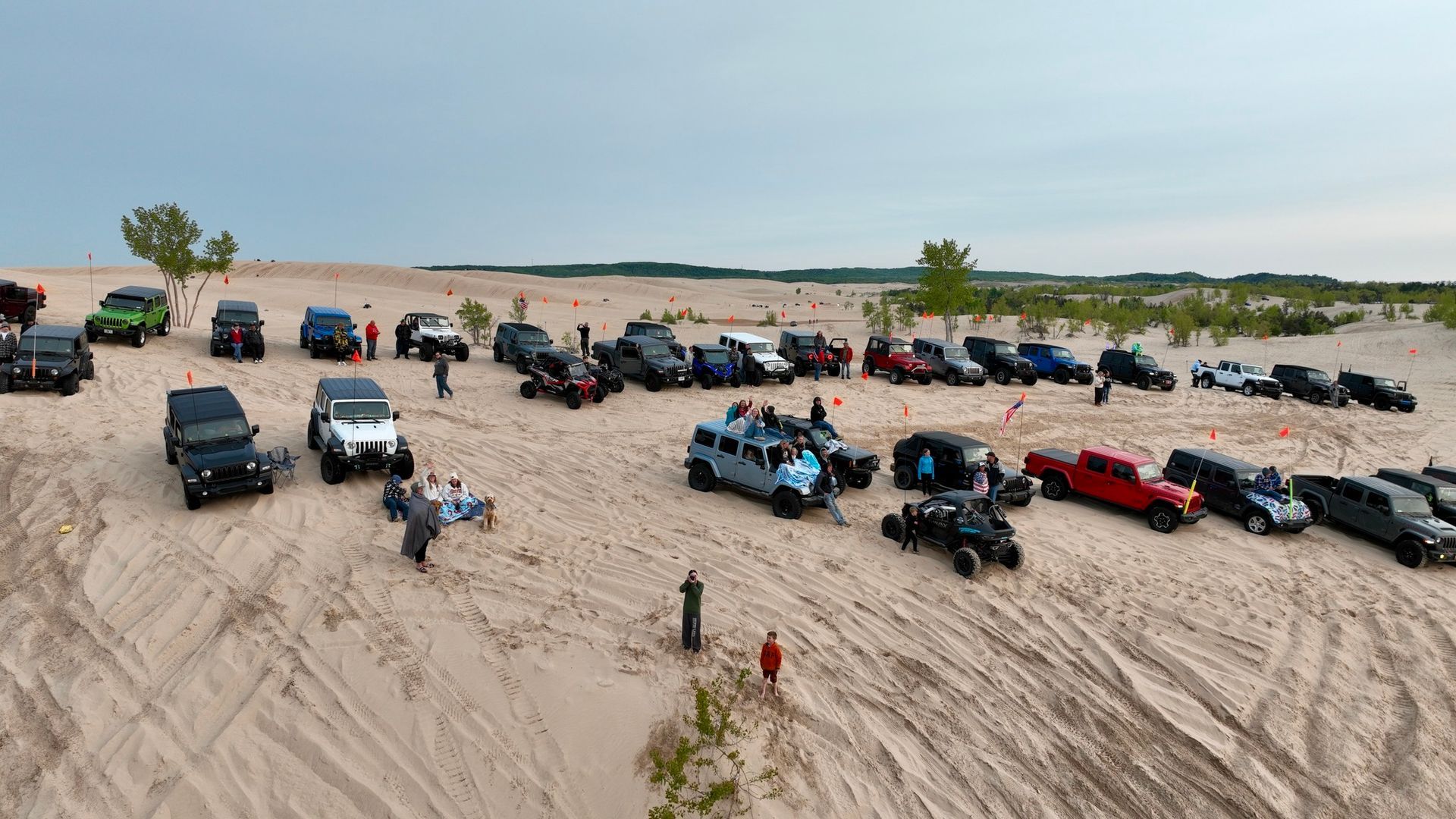 Vehicles and people on sand dunes under a cloudy sky.