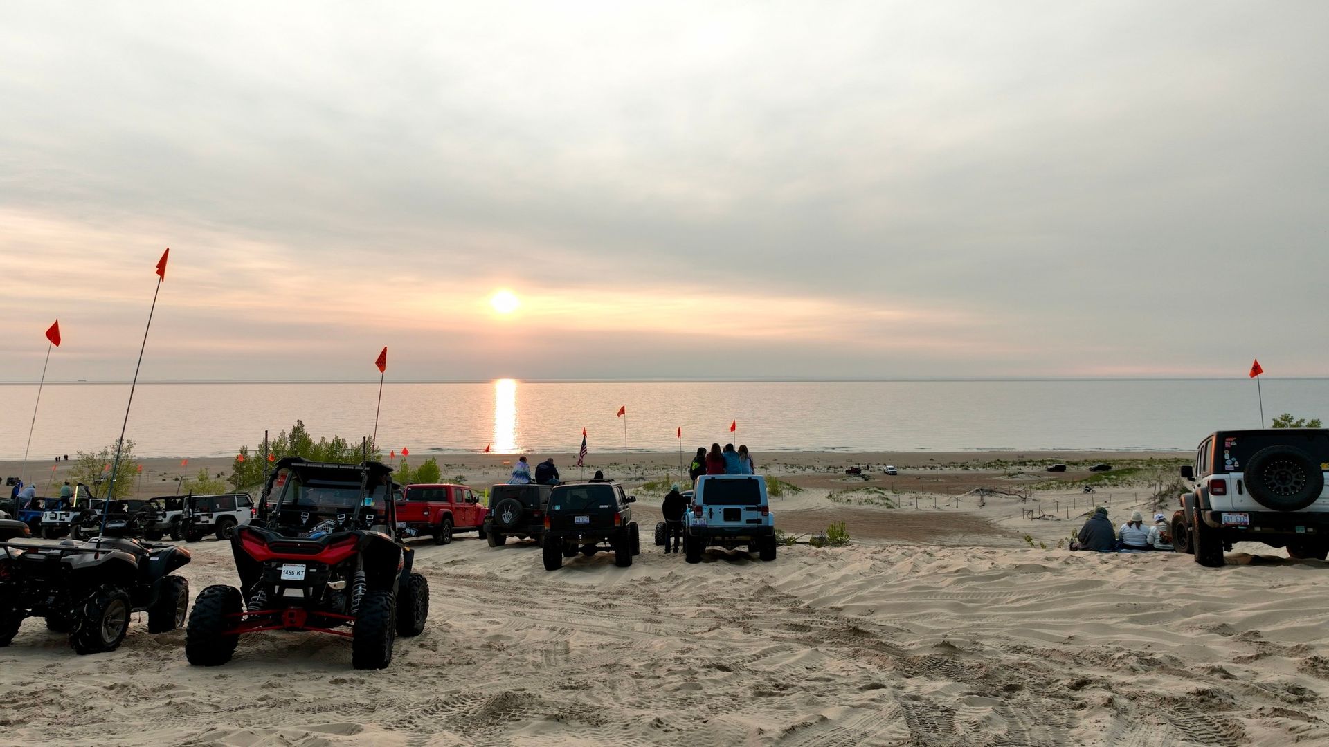 Off-road vehicles parked on a sandy beach, with a sunset over a body of water.