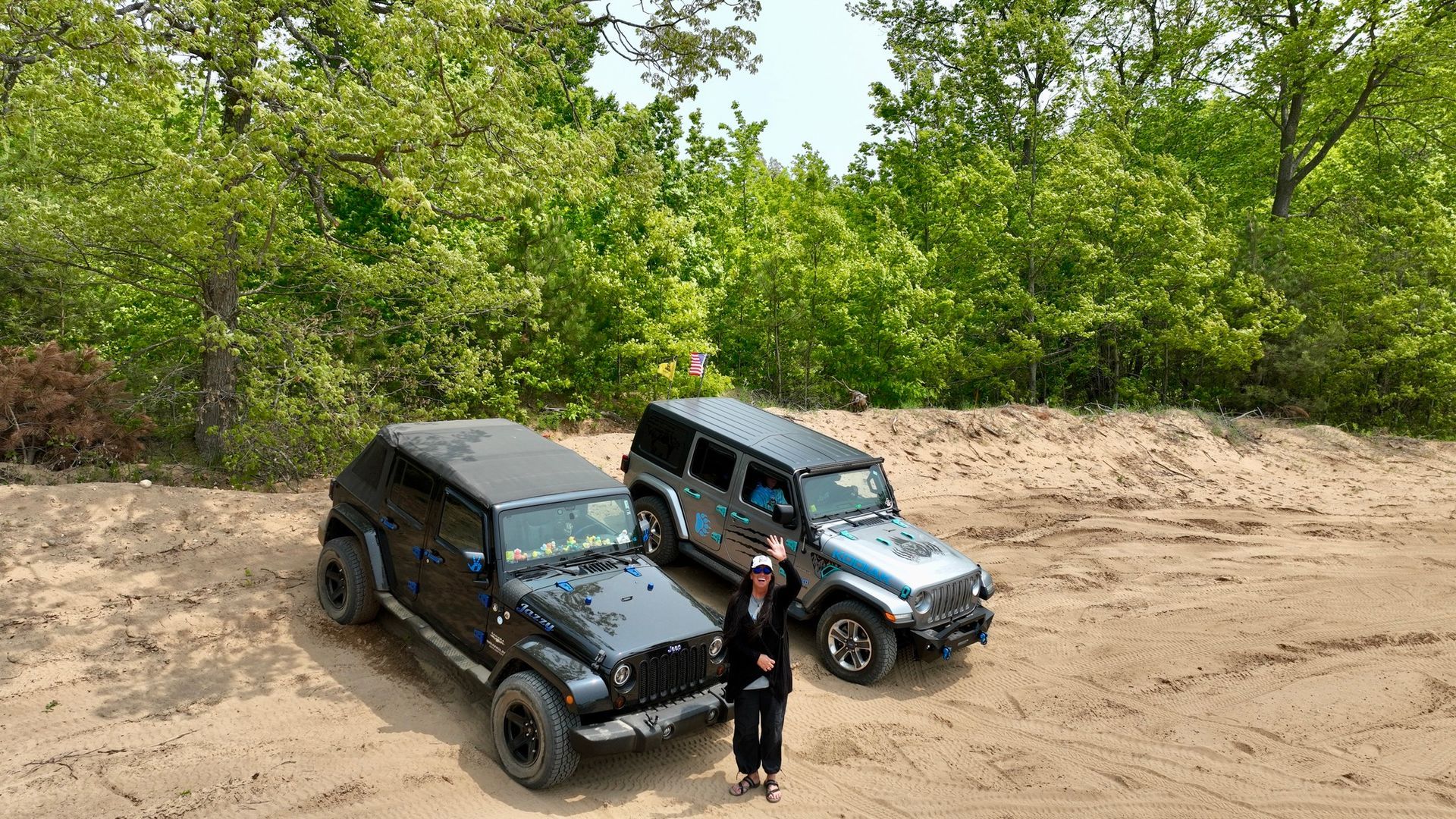 Two off-road vehicles parked on dirt with a person standing between them, trees in the background.