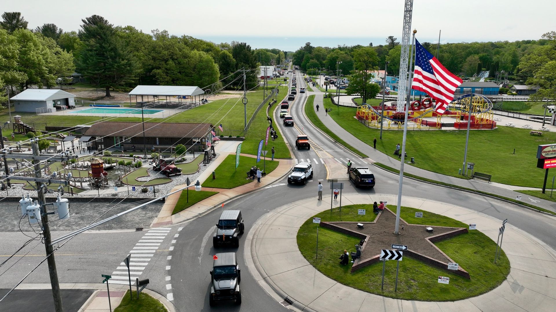 Cars on road approaching a roundabout with a star-shaped sculpture, large American flag, and buildings in the background.
