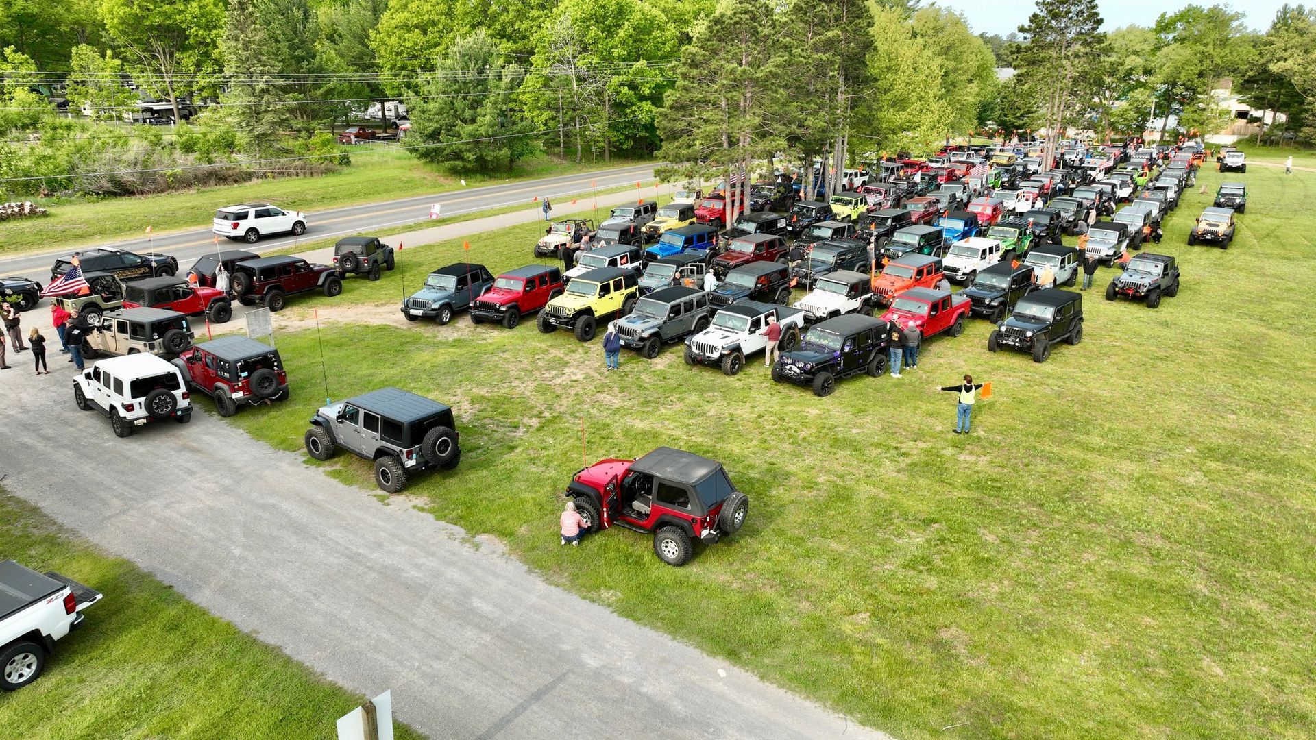 Large gathering of Jeeps on a grassy area; people standing near vehicles, some with tops off.