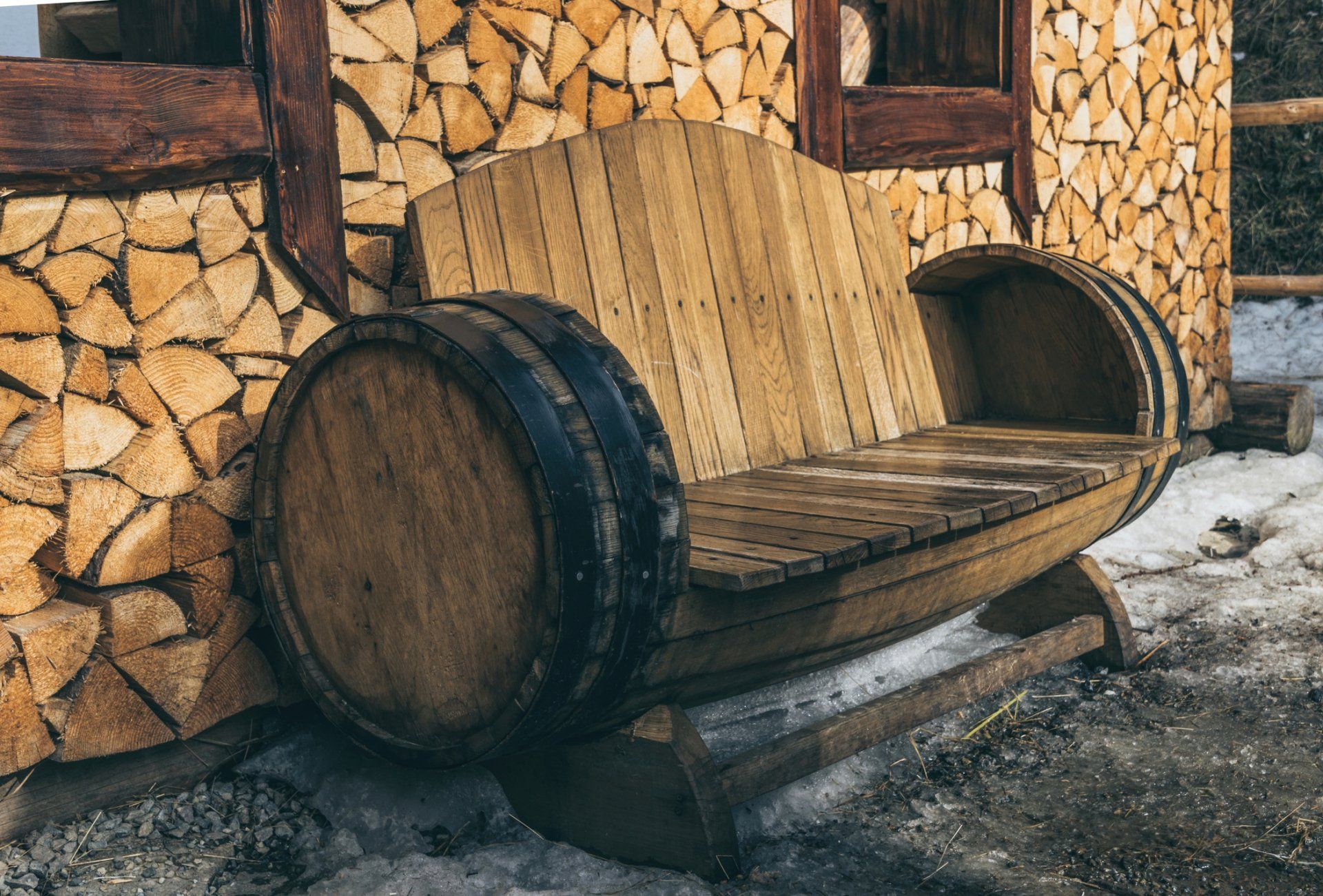 A wooden bench made out of wine barrels is sitting in front of a wooden building.