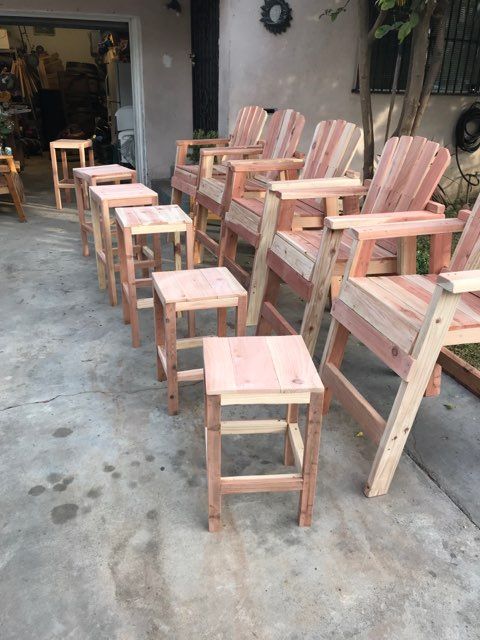 A row of wooden chairs and stools are lined up on a concrete surface.