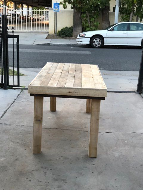 A wooden table is sitting on the sidewalk in front of a white car