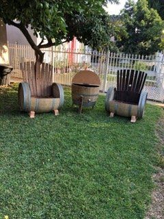 Three chairs made out of wine barrels are sitting in the grass.