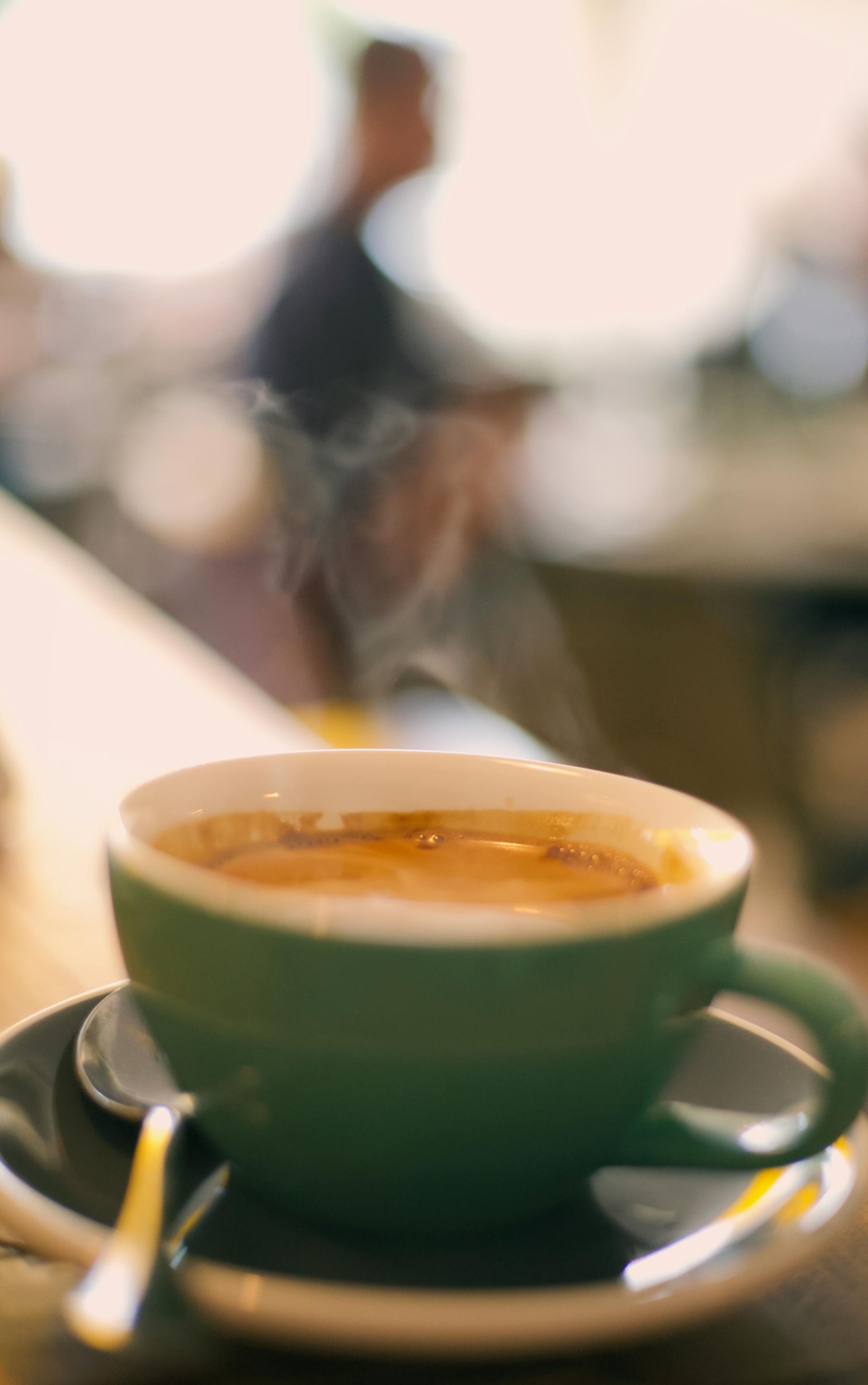 Green coffee cup and saucer on a table with a blurred café background