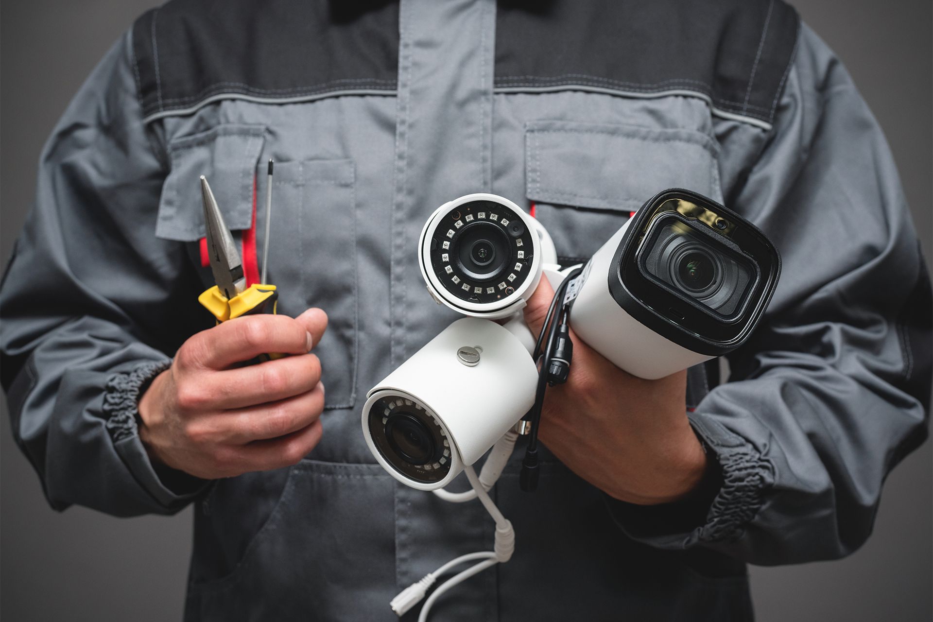 Technician in gray jumpsuit holds three white security cameras