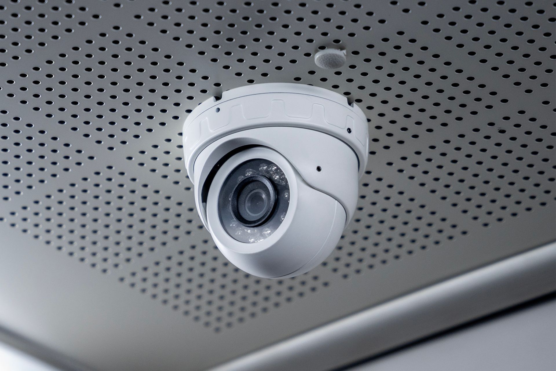 White security camera mounted on a perforated ceiling panel
