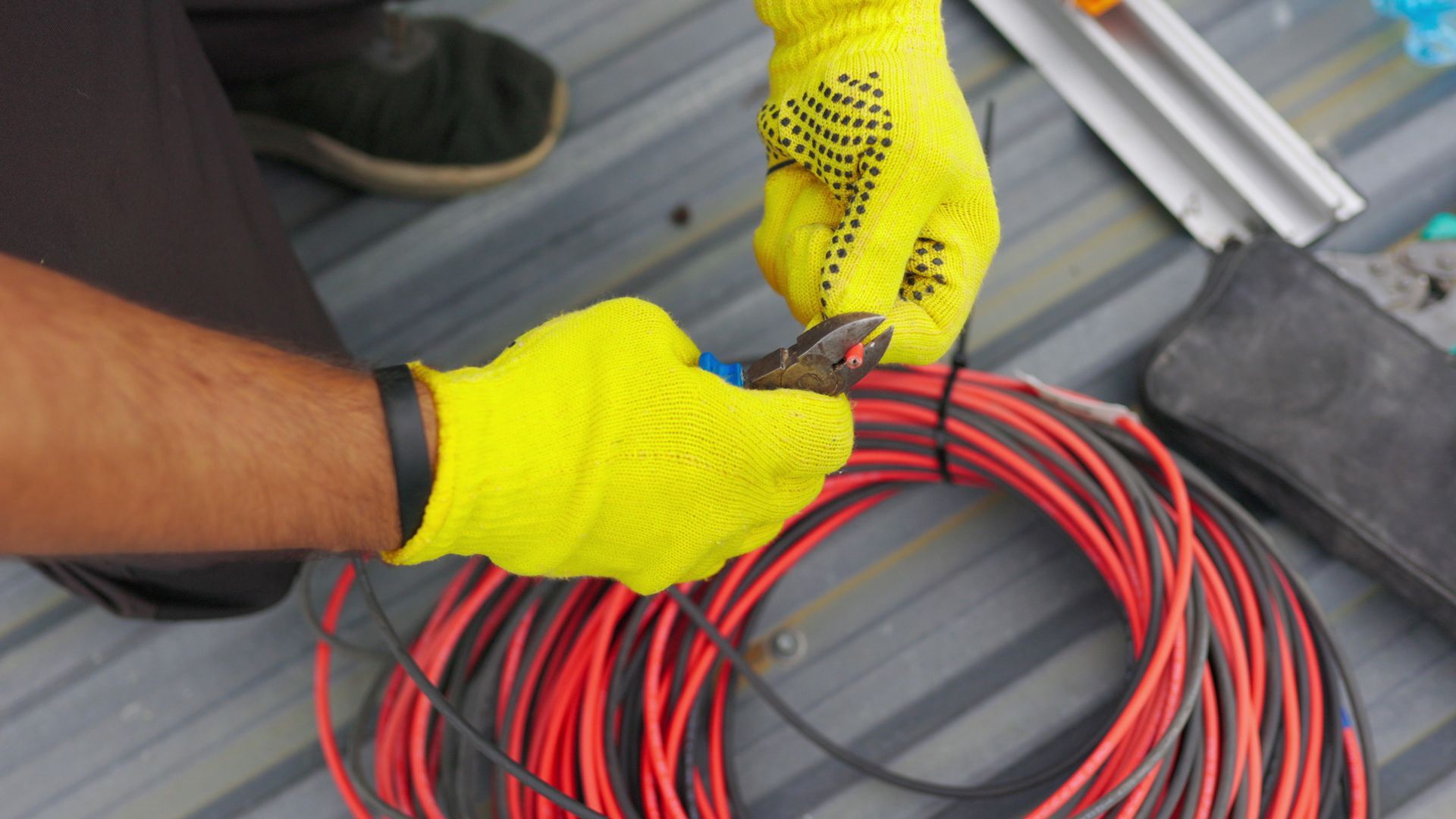 Person in yellow gloves cutting wires on a rooftop