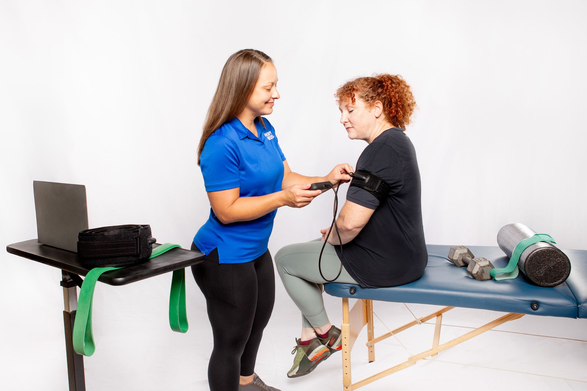 A healthcare provider measures a patient's blood pressure. They are in a clinic setting with exercise equipment.