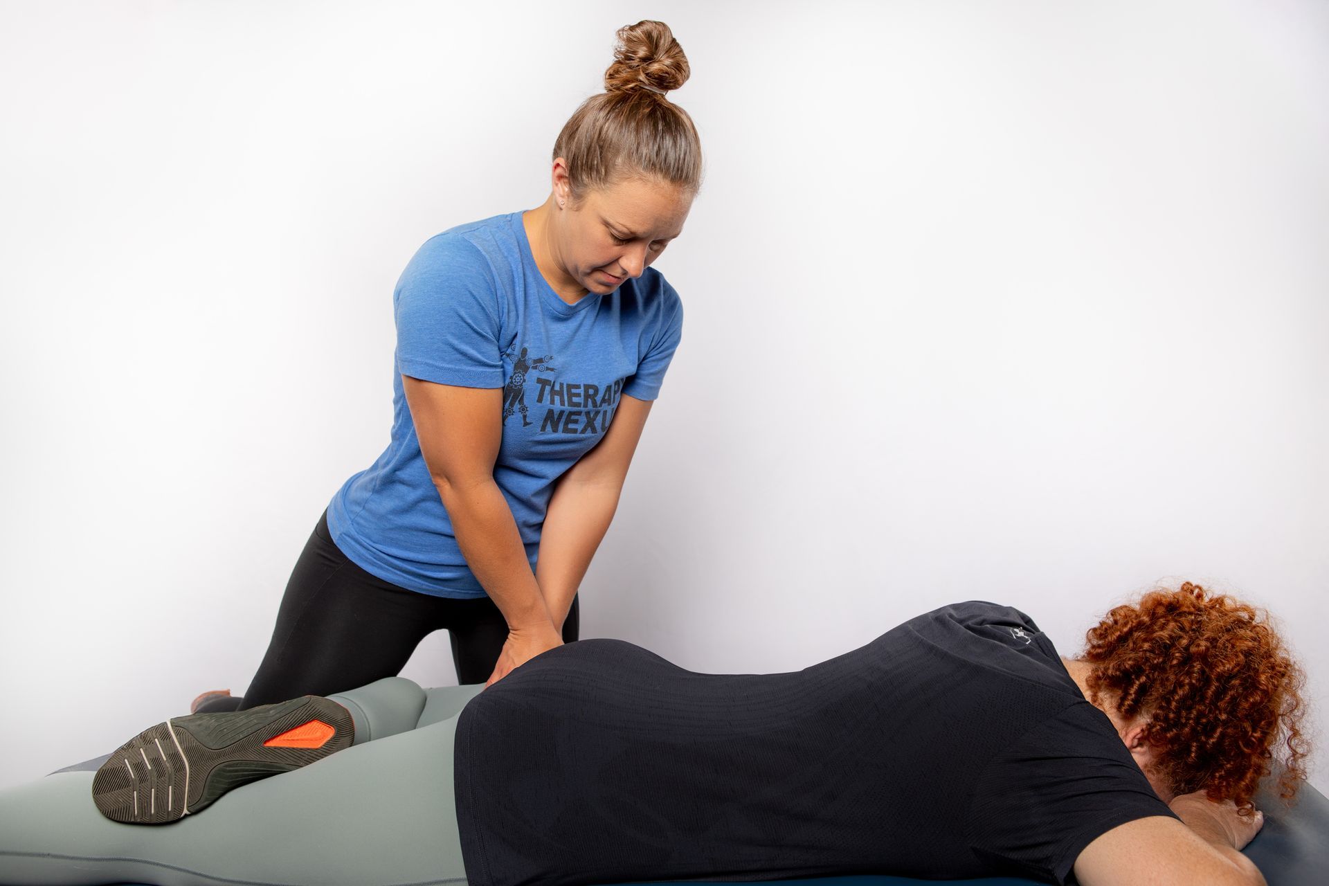 Woman in blue shirt assisting another person lying on a therapy table, hands on their lower back.