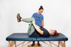 Therapist assists patient with leg exercise using resistance band on a treatment table.