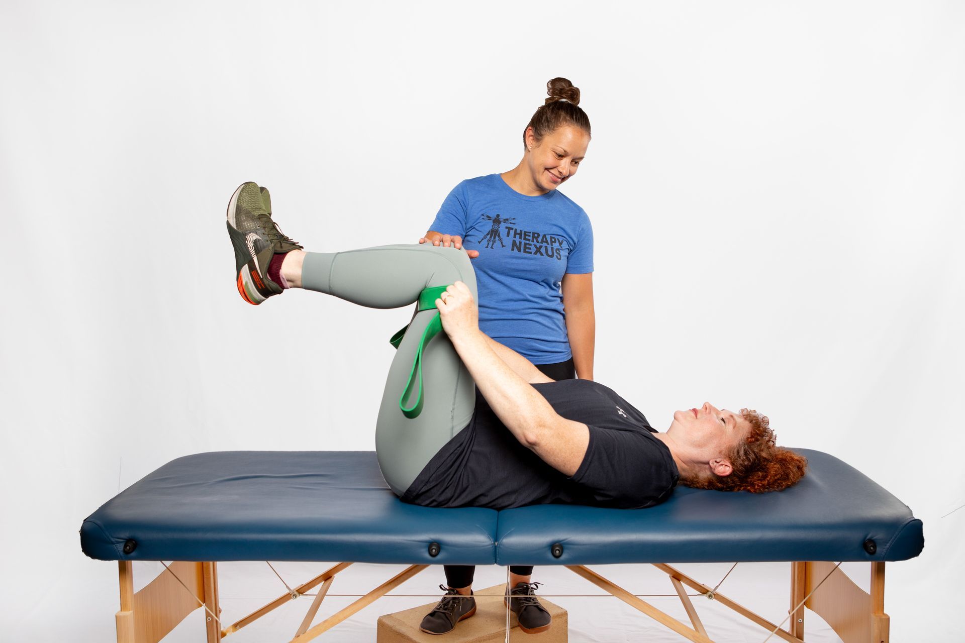 Therapist assists patient with leg exercise using resistance band on a treatment table.
