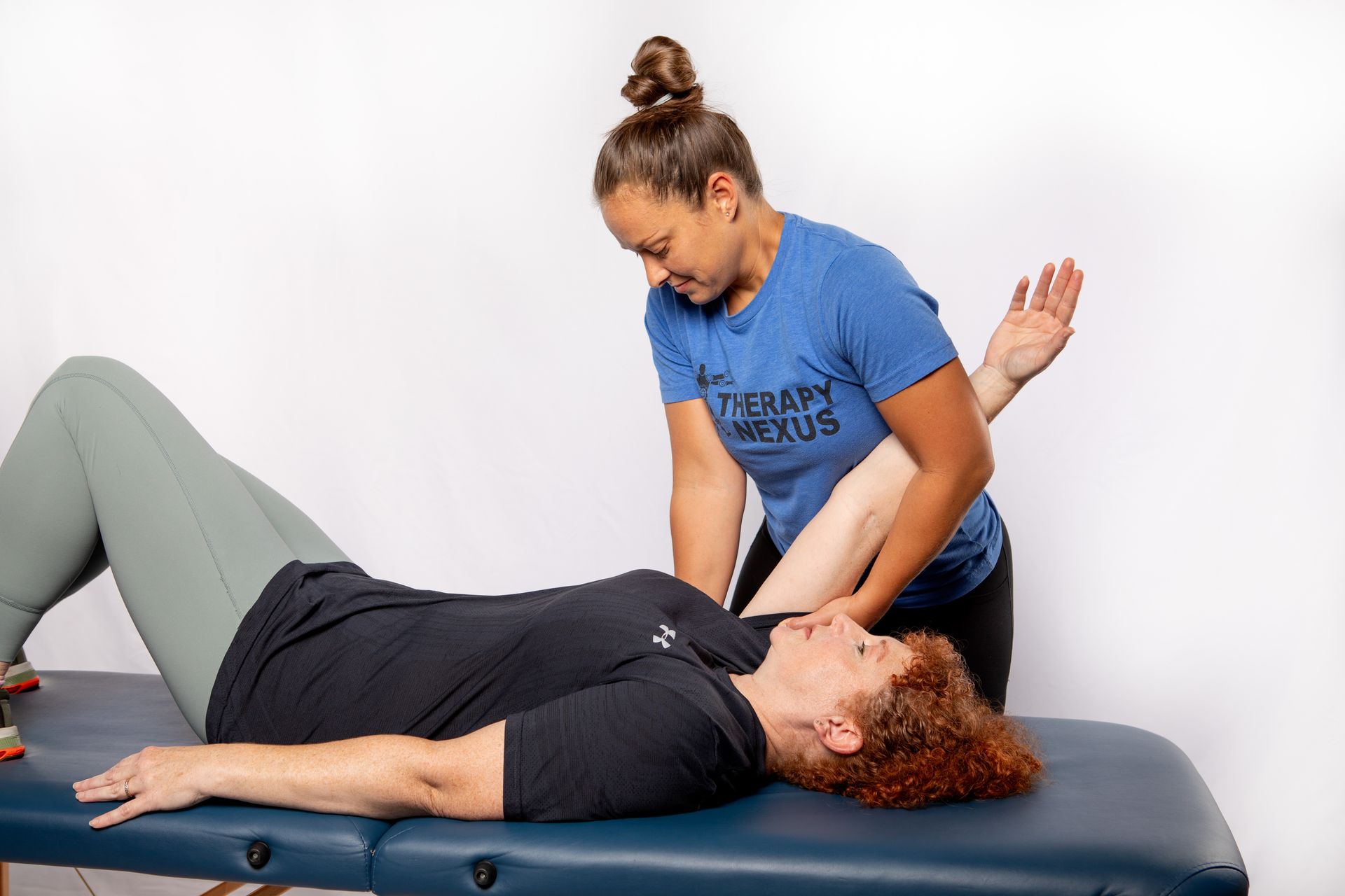 Woman lying on table with therapist manipulating her arm. White background.
