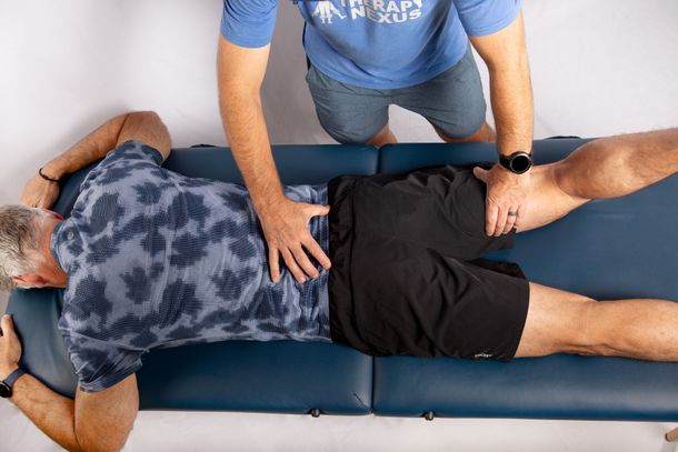 Man lying on a table, receiving a back assessment from a person in a blue shirt.