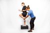 Woman stepping onto a box, assisted by another woman. They are in front of a white background.
