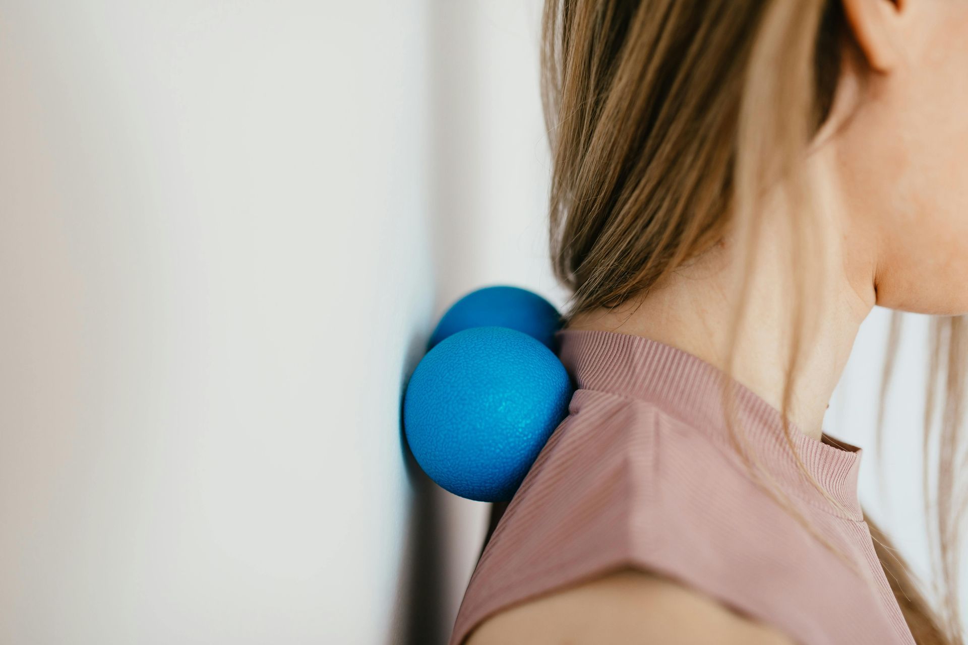 Woman using blue massage balls on neck against a white wall.