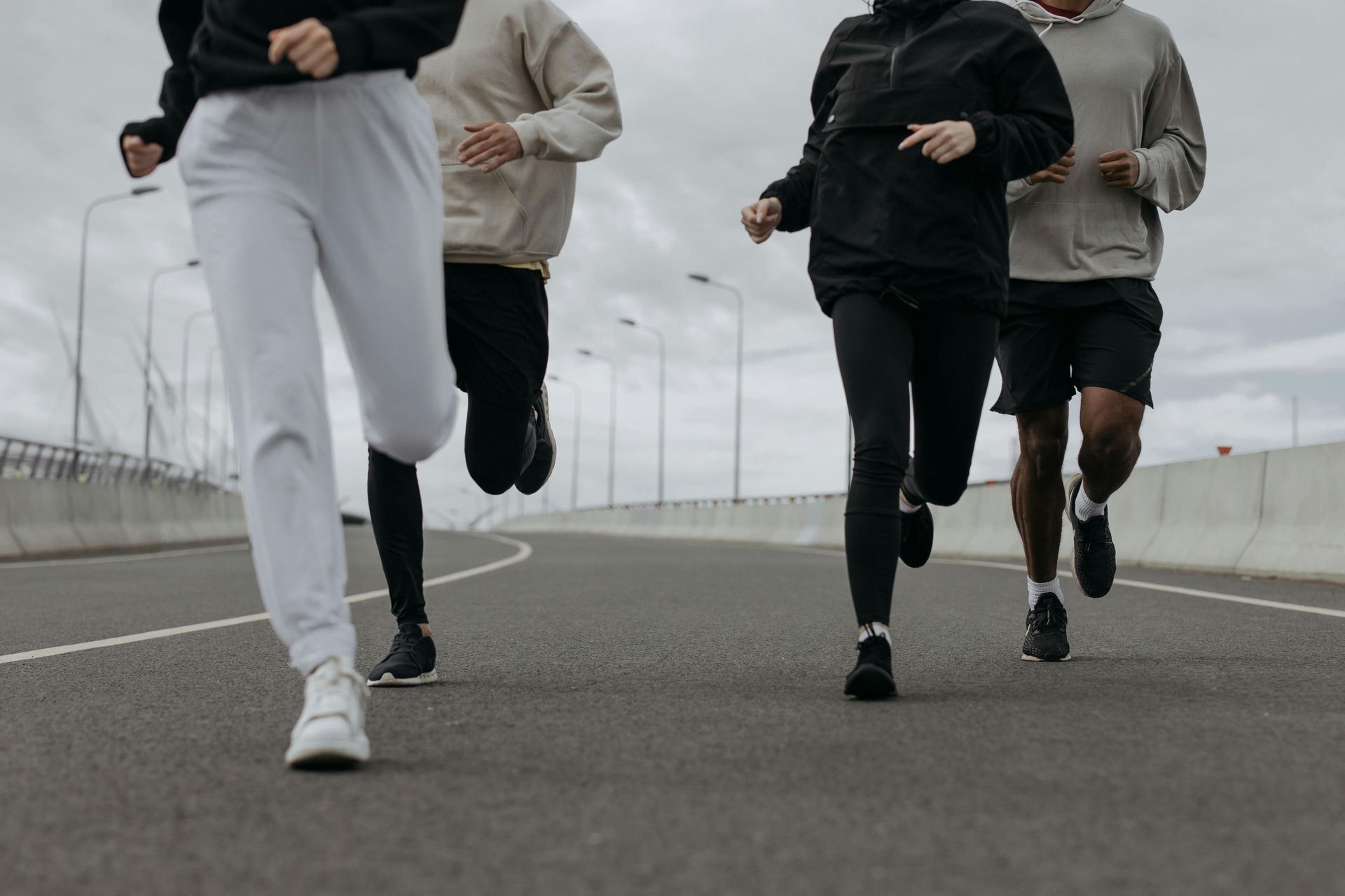 Four people running on a paved road beneath a cloudy sky.
