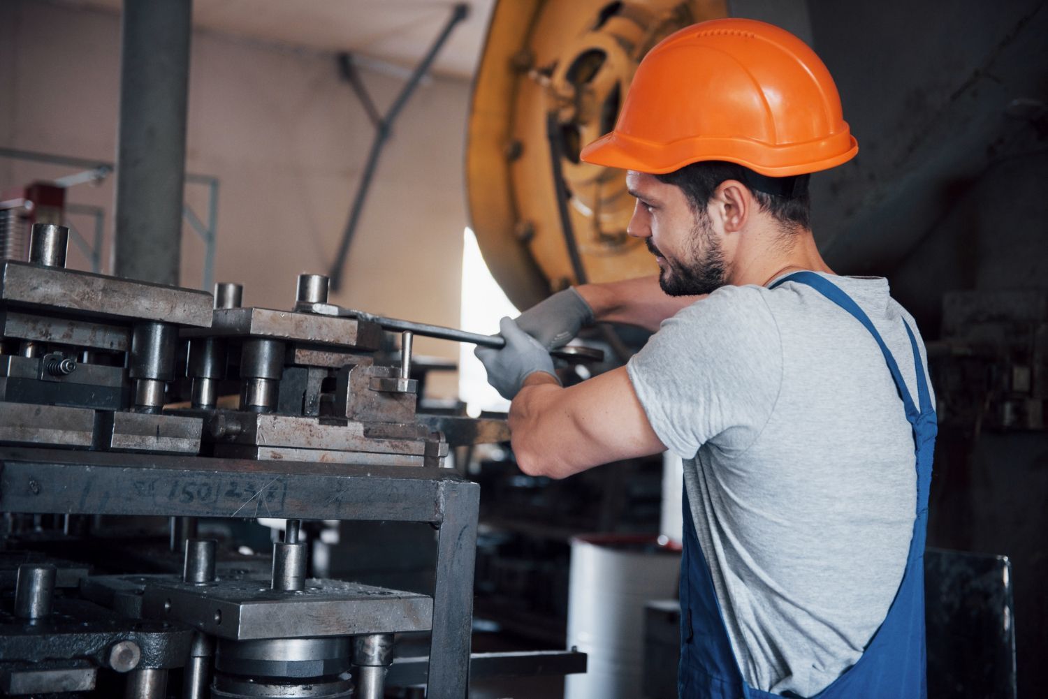 Trabajador con casco naranja manejando una máquina en un taller de fábrica.