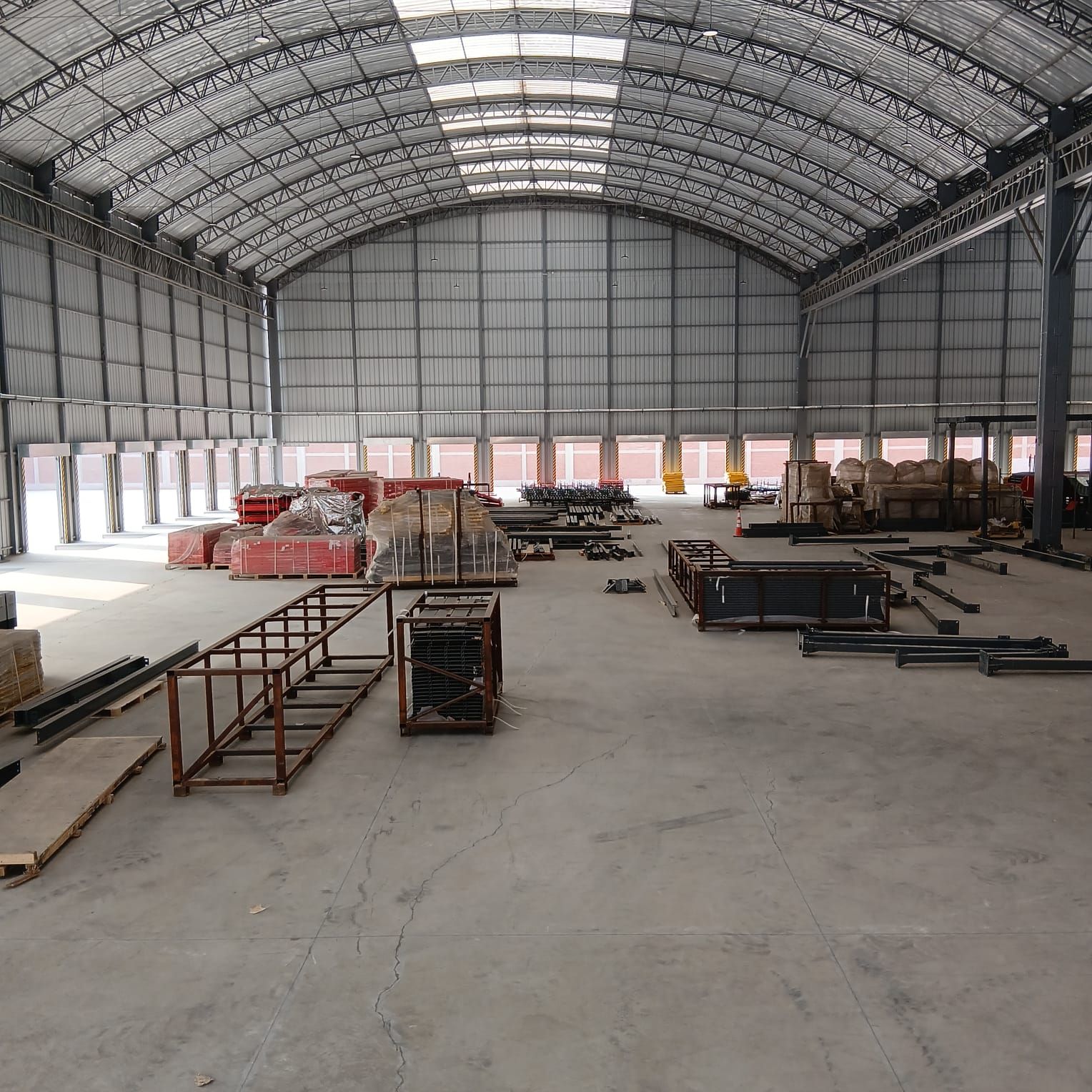 Taller industrial con trabajadores, estructuras metálicas rojas y grúas aéreas en una gran nave industrial.