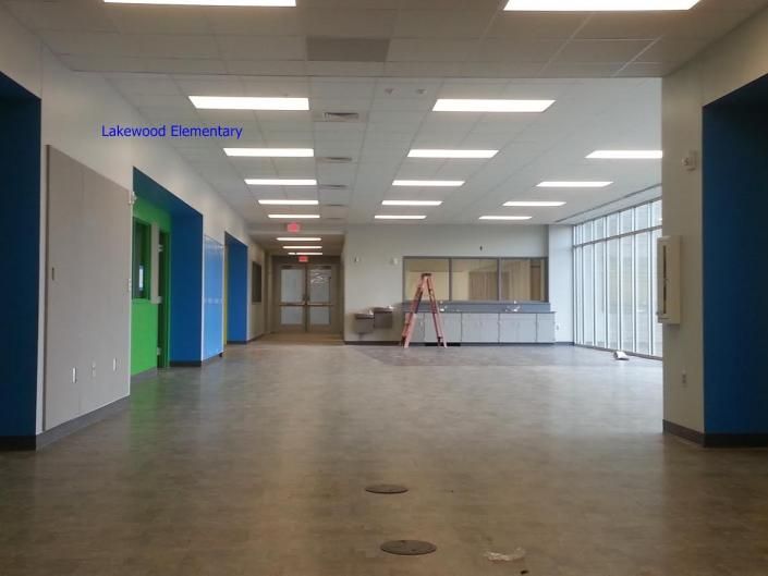 A modern school hallway with polished concrete floors, blue and green walls, and a ladder by a windowed partition.