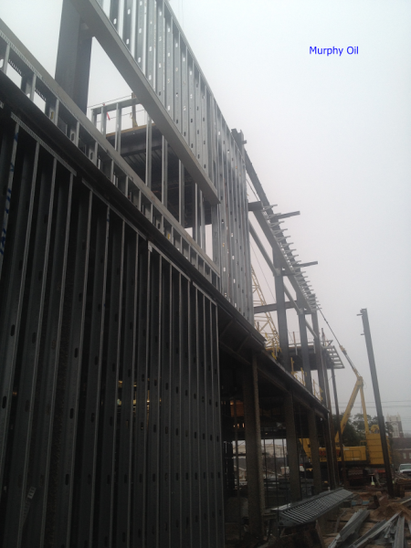 Steel framing of a multistory building under construction against a foggy sky, with a yellow crane visible.
