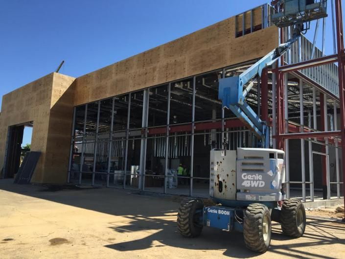 A blue Genie boom lift parked in front of a construction site with exposed metal framing and plywood wall panels.