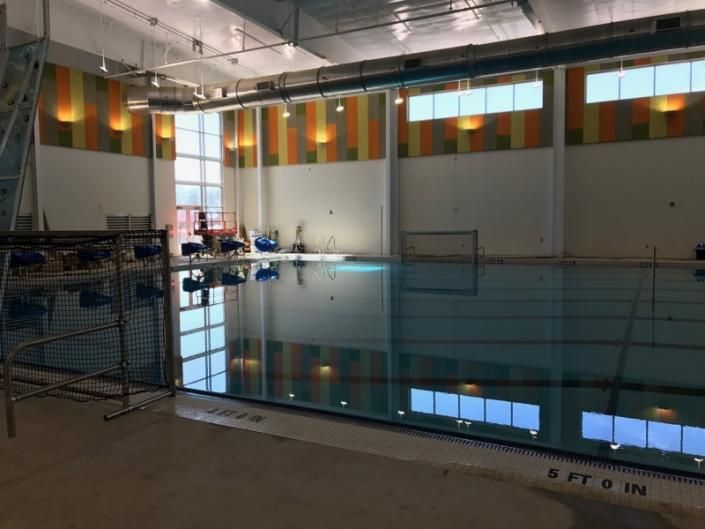An indoor swimming pool with colorful wall accents and large windows, reflecting light across the still water.