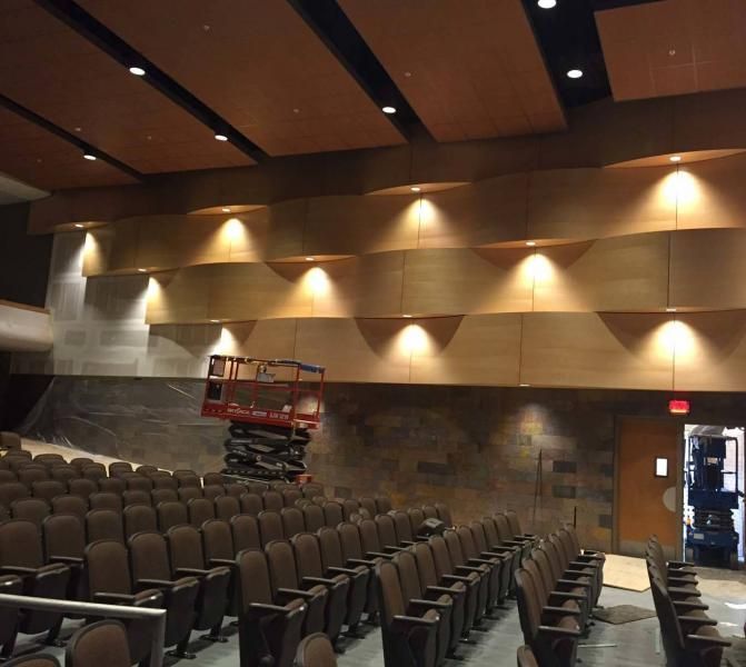 A modern auditorium with tiered seating, wood-paneled walls with recessed lighting, and a lift inside the room.