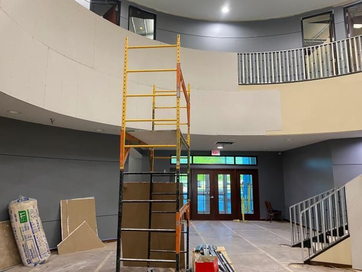 A tall scaffolding structure stands in the center of a building lobby under construction with bare walls and a staircase.
