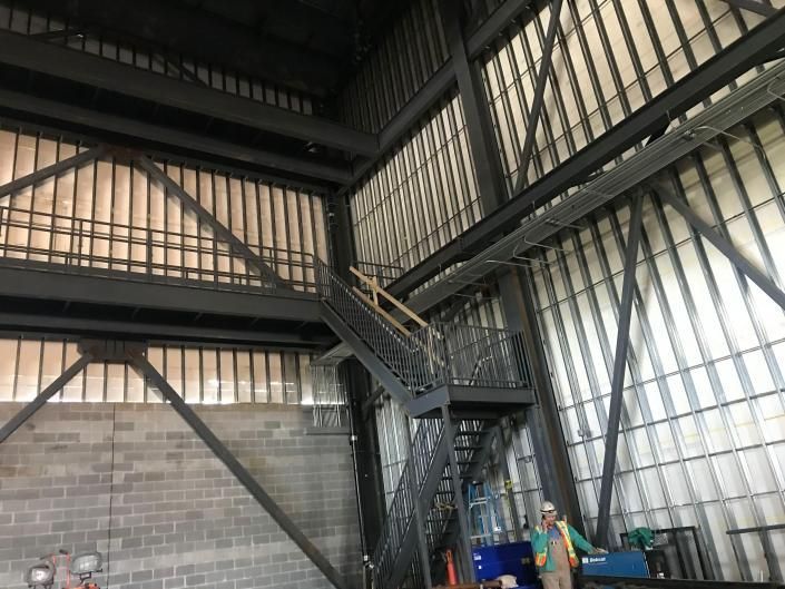A person in a high-visibility vest standing near a black metal staircase inside a tall industrial building.