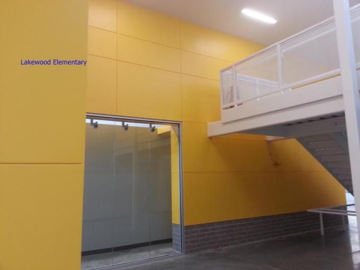 A bright yellow wall at Lakewood Elementary with a glass doorway and an elevated white staircase nearby.