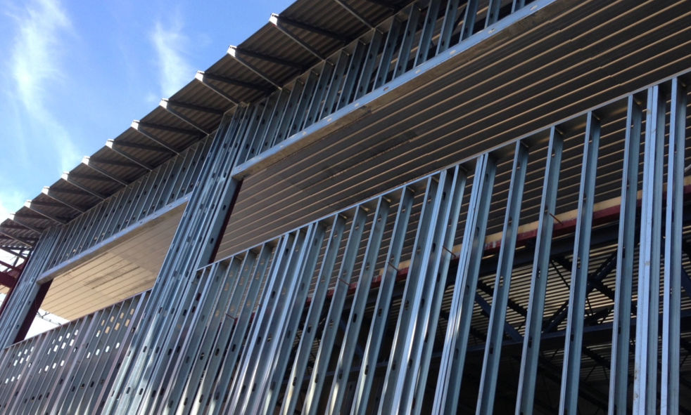 The metal frame structure of a building under construction, showing steel studs and a corrugated roof against a blue sky.