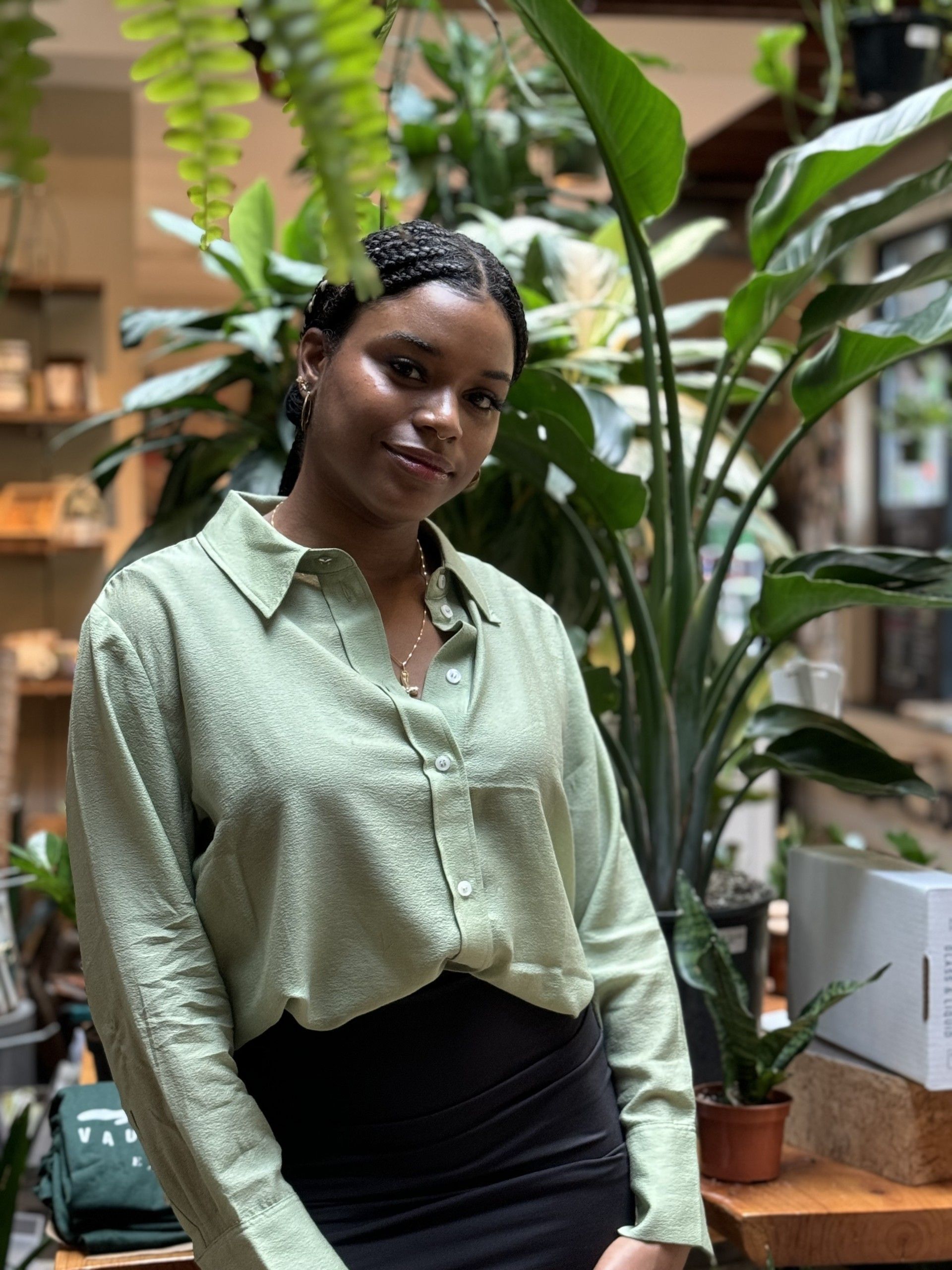 A woman in a green shirt and black skirt is standing in front of a bunch of plants. - WrightNow Counseling – Philadelphia, PA